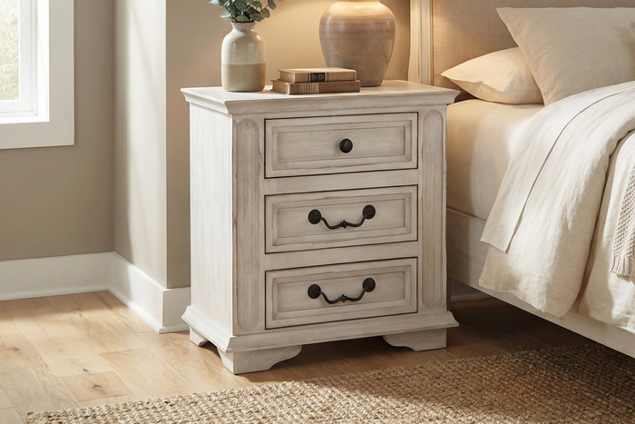 Neatly made bed with beige bedding and a matching nightstand in a bedroom setting.